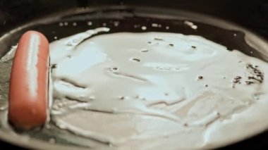 Mavi eldivenli bir el, sosislerin yarısını ayçiçeği yağıyla kaplı sıcak bir tavaya serer.