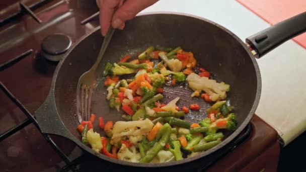 A mão caucasiana mexe verduras em uma panela de ato de fritar com garfo de aço inoxidável fritando, close-up — Vídeo de Stock