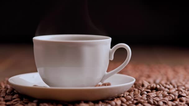 Steam rises from a hot cup of coffee against a background of roasted coffee beans — Stock Video