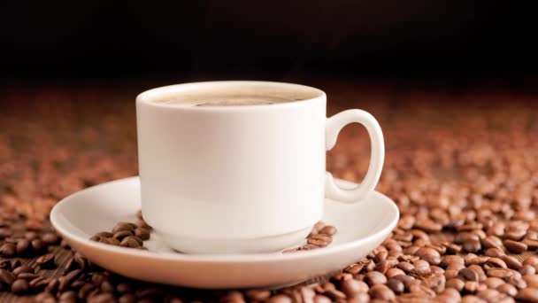 Dampf steigt aus einer Tasse heißen Kaffees vor dem Hintergrund gerösteter Kaffeebohnen auf. — Stockvideo