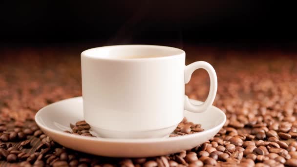 Steam rises from a mug of hot coffee against a background of roasted coffee beans — Stock Video