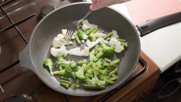 Mujer caucásica revolviendo verduras fritas en aceite hirviendo con tenedor — Vídeo de stock