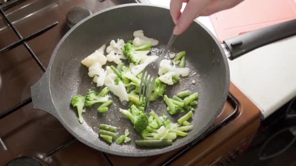 Kaukasisk kvinna som rör om och steker grönsaker i kokande olja med gaffel — Stockvideo