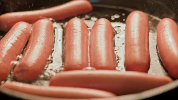 A hand in a blue glove rearranging sausages in a hot frying pan covered with sunflower oil — Stock Video