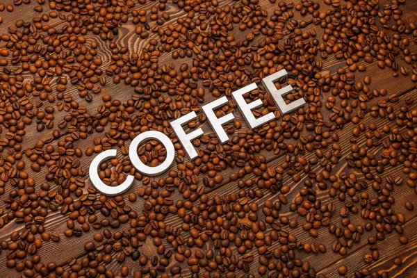 The word coffee laid with silver letters on wooden board surface covered with roasted coffee beans — Stock Photo, Image