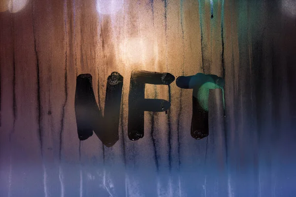 A palavra NFT - token não fungível escrito à mão em vidro de janela nebuloso à noite — Fotografia de Stock