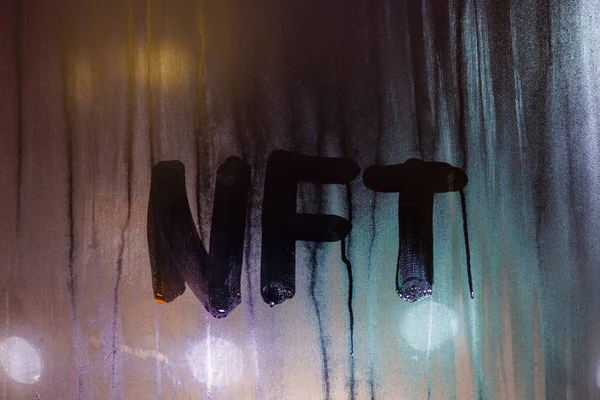 Слово NFT - нерозчинний жетон, написаний вручну на туманному склі вікна вночі — стокове фото