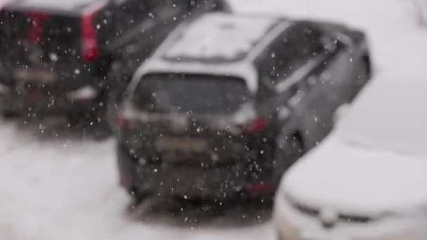Slow-mo snow falling on blurred background of parked cars at cloudy day with selective focus — Stockvideo