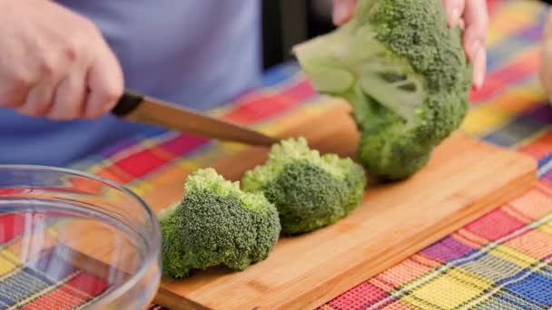 Elder caucasian woman cutting raw green broccoli on bamboo cutting board — Stock Video