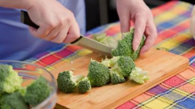 Yaşlı beyaz kadın bambu kesme tahtasıyla çiğ yeşil brokoli kesiyor.