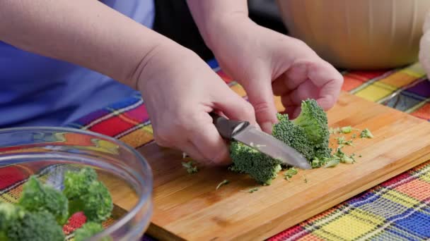 Elder caucasian woman cutting raw green broccoli on bamboo cutting board — Stockvideo