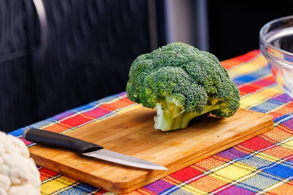 A head of green broccoli on a pink plastic cutting board, and colorful towel underneath — Stockfoto