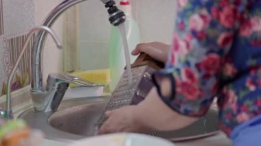 Beyaz kadın mutfakta bulaşıkları sarı süngerle yıkıyor.