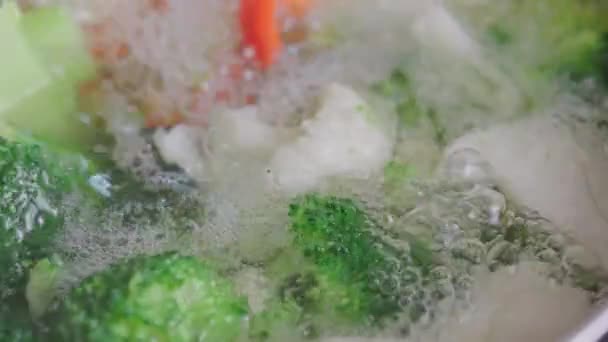 Stainless steel spoon stirring and removing scum foam out from boiling broccoli, cauliflower and red bell pepper extreme close-up with slow motion — Stockvideo