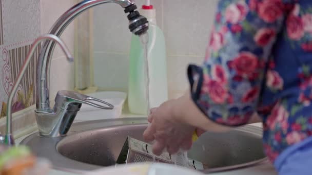 Ηλικιωμένη καυκάσια γυναίκα πλένει πιάτα με κίτρινο σφουγγάρι στην κουζίνα — Αρχείο Βίντεο