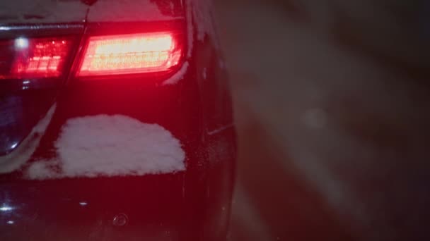 Rotes Rücklicht eines schwarzen Autos in der Nacht Straße im Winter Schneefall — Stockvideo