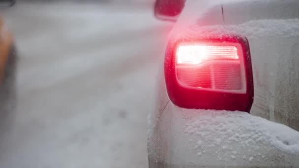 Red tail light of black car at day street in winter snowfall — Video Stock