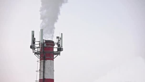 Thermal power station pipe at winter with outgoing smoke, steam and isicles on telecommunication antennas — Wideo stockowe