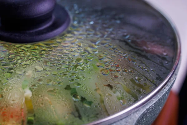 Vegetables in frying pan covered with glass lid with water condensation drops on inner surface — Stockfoto