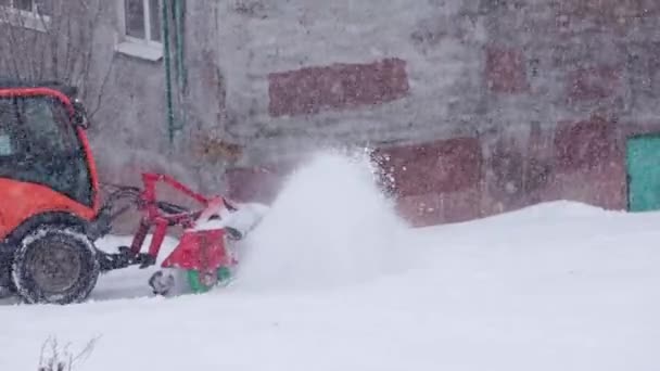 Traktor merah defocused dengan bajak salju membersihkan salju trotoar di musim dingin badai siang hari — Stok Video