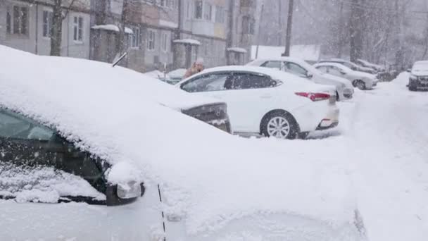 Zimowy dzień zamieć w rosyjskiej ulicy z zaparkowanymi samochodami wzdłuż rosyjskiego budynku khrushchevka — Wideo stockowe