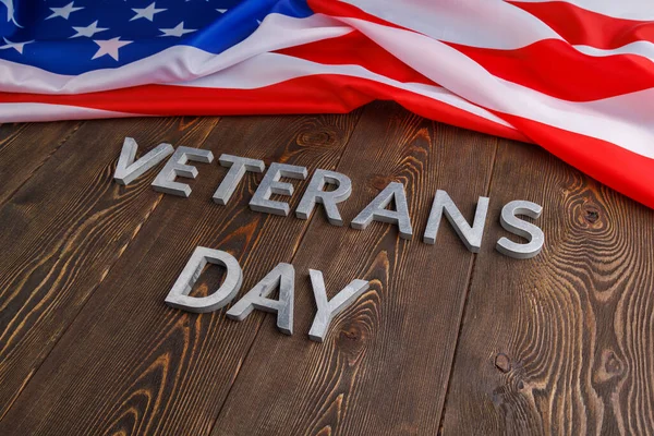 The words veterans day laid with silver metal letters on wooden board surface with crumpled usa flag at right side with diagonal perspective — Zdjęcie stockowe