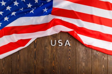Amerika Birleşik Devletleri 'nin buruşuk bayrağı altında ahşap tahta yüzeyine gümüş metal harflerle yazılmış ABD sözcüğü.