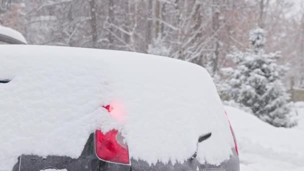 Back side of snow covered black hatch back car at daylight snowfall, engine strated remotely — Vídeo de Stock