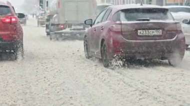 cars drive on a snow-covered road in a snowfall with heavy snow ejection from under the wheels