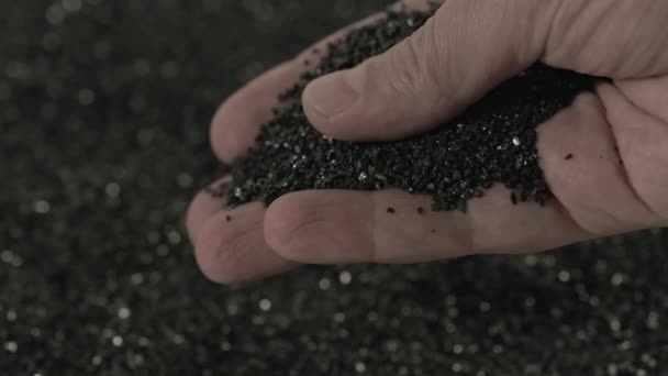 A mão caucasiana nua segurando e derramando carvão ativado preto pó de carvão de coco de pequena fração em câmera lenta — Vídeo de Stock