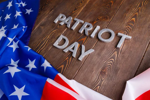 Slova vlastenecký den položený stříbrnými kovovými písmeny na dřevěném povrchu desky se zmačkanou vlajkou USA — Stock fotografie