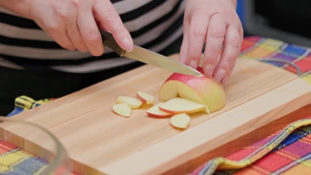 Starší žena řezané červené jablko s nožem na dřevěné řezací desce na kuchyňském stole — Stock video