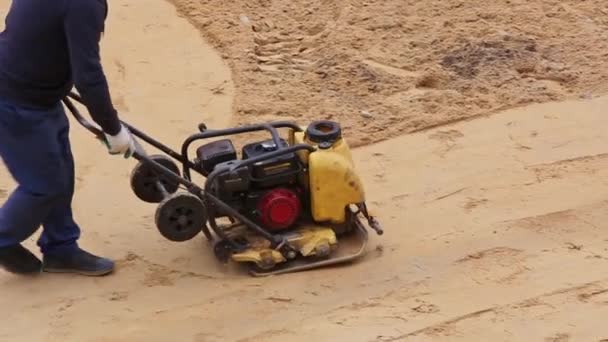 Работник с вибрационной пластиной уплотнитель таран песок на строительной площадке перед мощения — стоковое видео