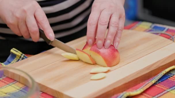 Starší žena řezané červené jablko s nožem na dřevěné řezací desce na kuchyňském stole pro jablečný koláč — Stock video