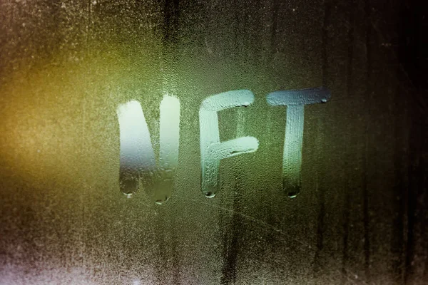A palavra NFT - token não fungível escrito à mão em vidro de janela nebuloso à noite — Fotografia de Stock