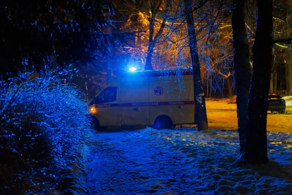 Российская машина скорой помощи едет по улице за кустами в зимнюю ночь — стоковое фото