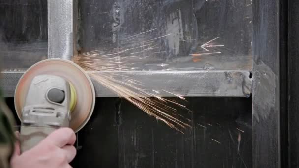 Caucasian hand cleaning of welded seams with an angle grinder with a flap disc on welded metal construction close-up with long spark trails, slow motion — Stock Video