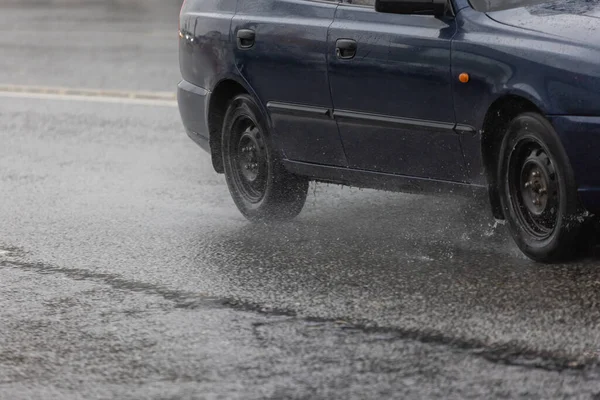Donkerblauwe budget auto beweegt op regenachtige dag op asfaltweg — Stockfoto