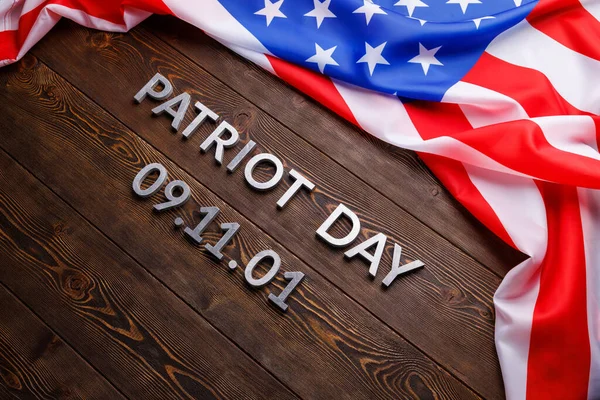 Slova vlastenecký den položený stříbrnými kovovými písmeny na dřevěném povrchu desky se zmačkanou vlajkou USA — Stock fotografie