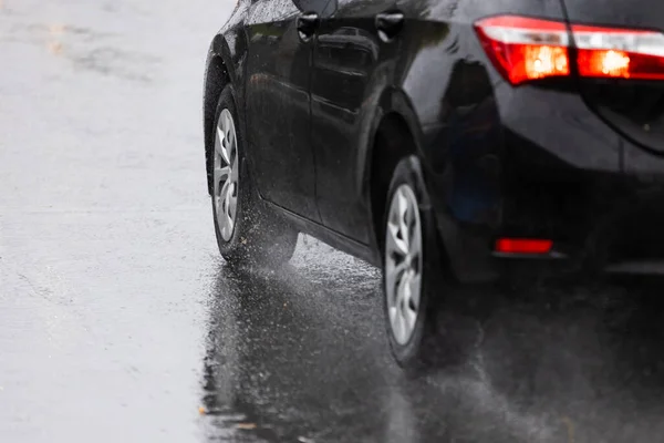 Regenwater splash flow van wielen van zwarte auto beweegt snel in daglicht stad met selectieve focus — Stockfoto