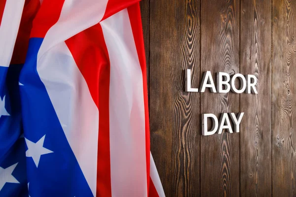 words labor day laid with silver metal letters on wooden surface with crumpled USA flag on left side