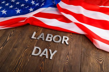 Tahta yüzeyde gümüş metal harflerle, sol tarafında buruşuk Amerikan bayrağıyla...