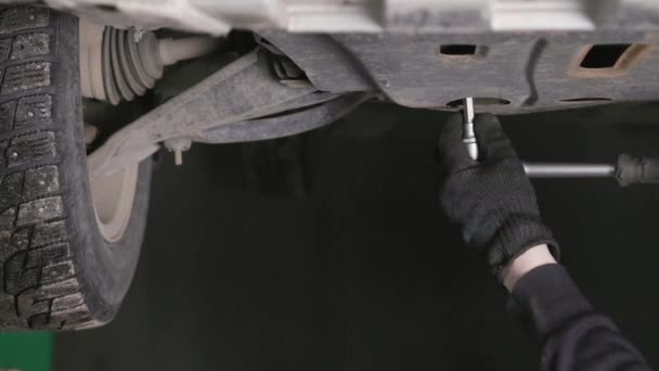 Μηχανικός ξεβιδώνει το βούλωμα του τηγανιού πετρελαίου μηχανών κάτω από το αυτοκίνητο κατά τη διάρκεια της αλλαγής πετρελαίου — Αρχείο Βίντεο