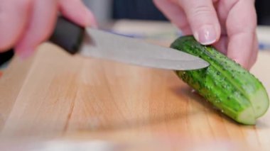 senior caucasian woman cut a green cucumber on wooden cutting board