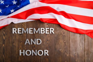 words remember and honor laid with silver metal letters on wooden background with USA flag above