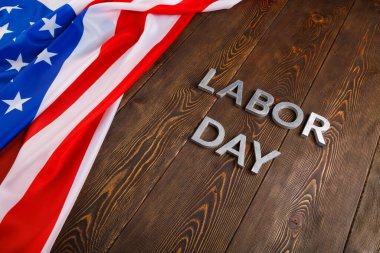 Tahta yüzeyde gümüş metal harflerle, sol tarafında buruşuk Amerikan bayrağıyla...