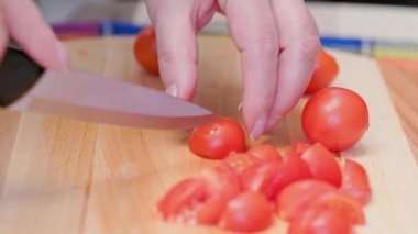 senior caucasian woman cut red cherry tomatoes on wooden cutting board