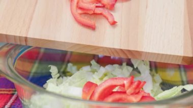 caucasian woman adding cut red bell pepper into bowl with cut chinese cabbage