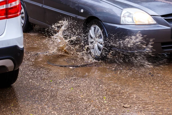water splashes from car wheel passing summer puddle around manhole cover