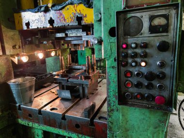 dirty used low tech stamping press in dark environment with large russian control panel